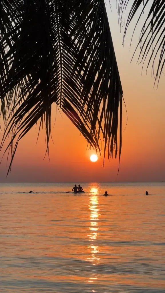 Sonnenuntergang über dem Meer, gerahmt von Palmenwedeln, mit Menschen im Wasser.